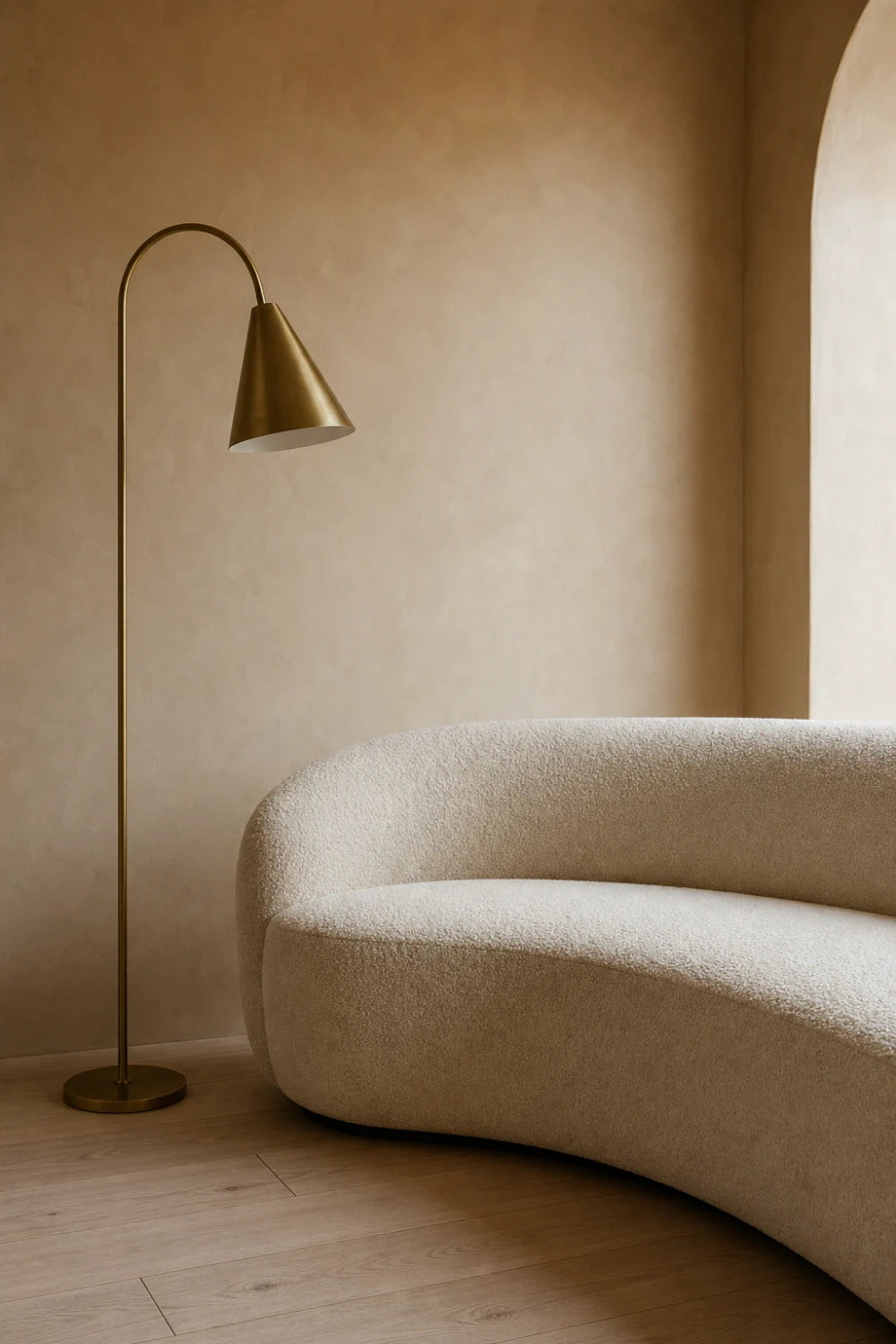 Curved cream boucle sofa beside an unlit brass floor lamp against a softly lit limewash wall.